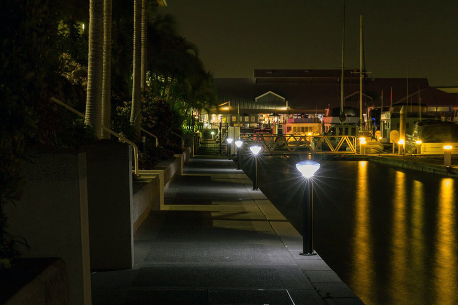 Architectural lit bollards dot the front of a marina and caution people away from the edge