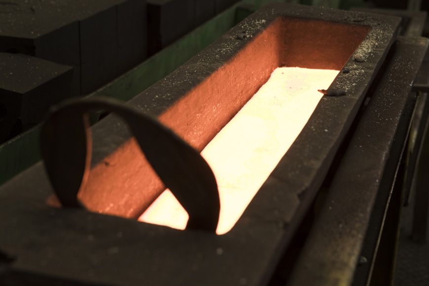 Glowing molten metal fills a sturdy metal form that will cool into an ingot