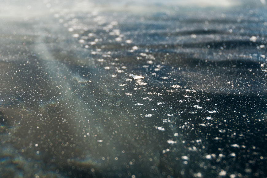 The pattern of a studded tire is left in the dark frozen ice of a lake