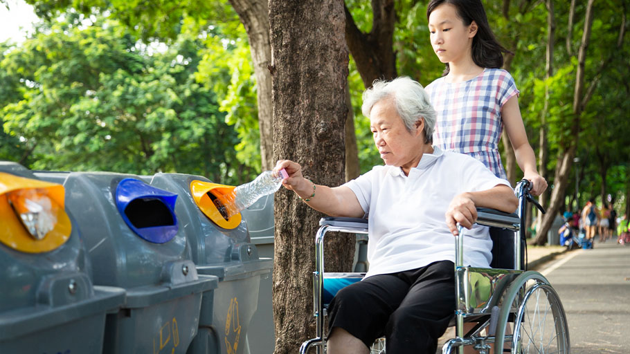 A young girl pushing a woman in a wheelchair to access public garbage bins