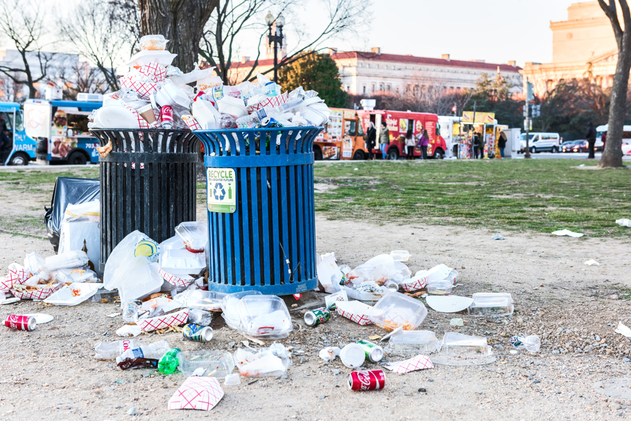 Overflowing garbage bins in front of food trucks.