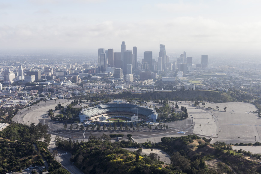 Arial picture of Dodger Stadium surrounded by a huge parking lot and smoggy city skyline