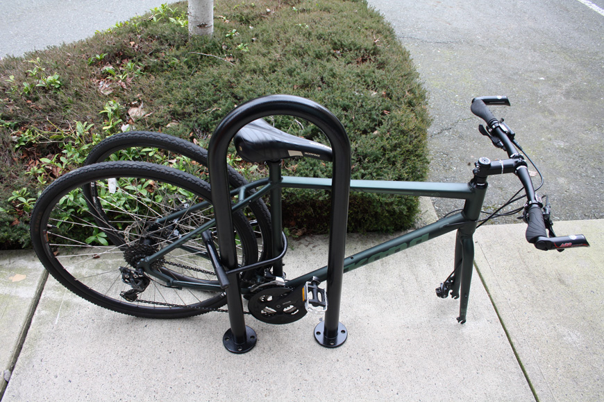 A green bike’s front tire is removed and locked with the back tire to an outdoor bicycle rack