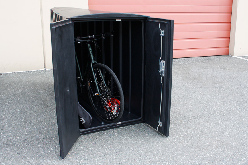 An open black bike locker contains a bike, a helmet, and a pannier.